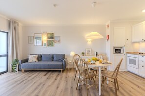 A modern living room with a sofa, dining table, chairs, and a kitchen area with cabinets and appliances. - #319 Cozy 1 Bedroom Apartment | Pool & Relaxation (Albufeira)