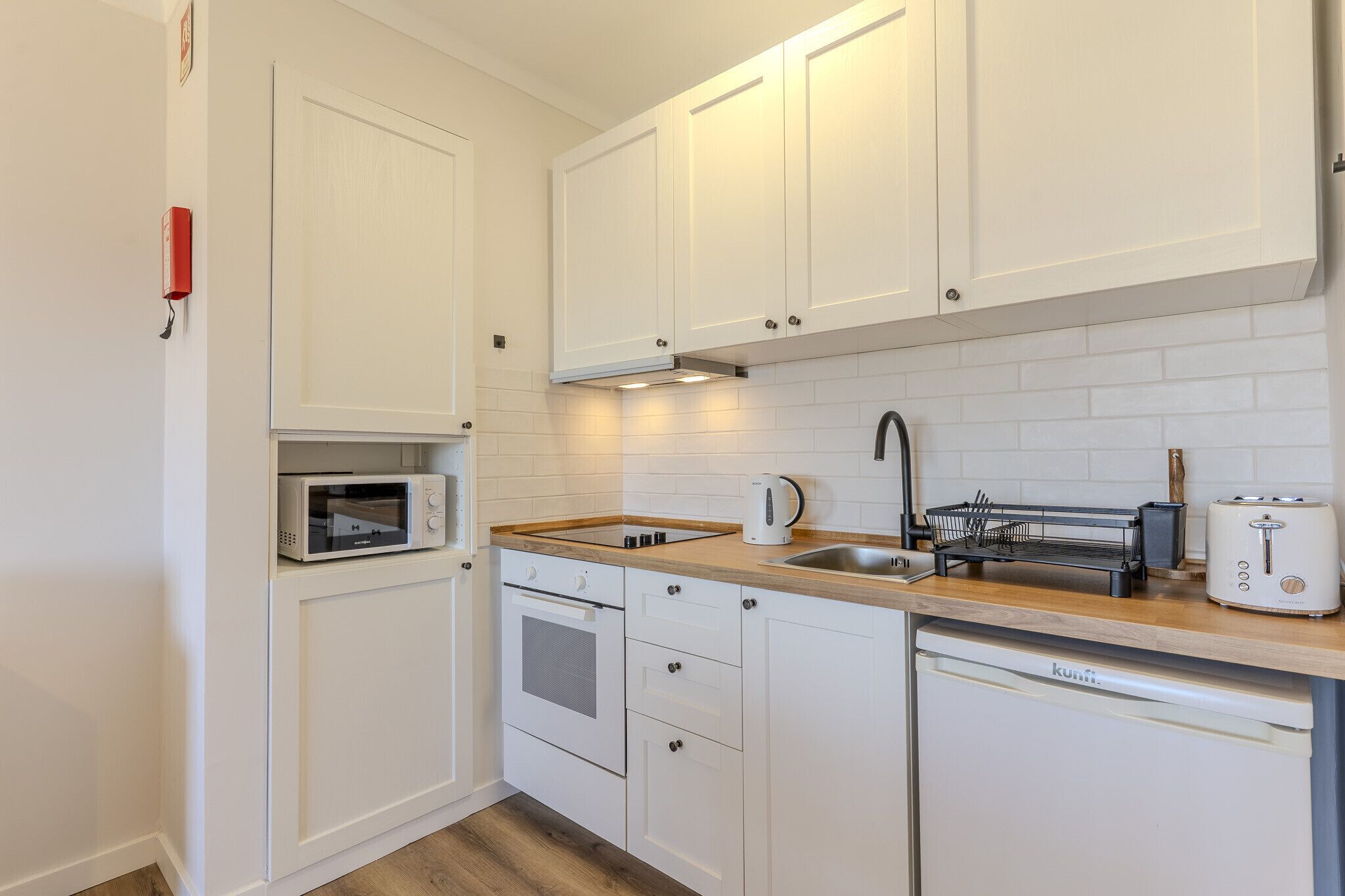 Una cocina compacta con armarios blancos, microondas, tostadora y lavamanos.