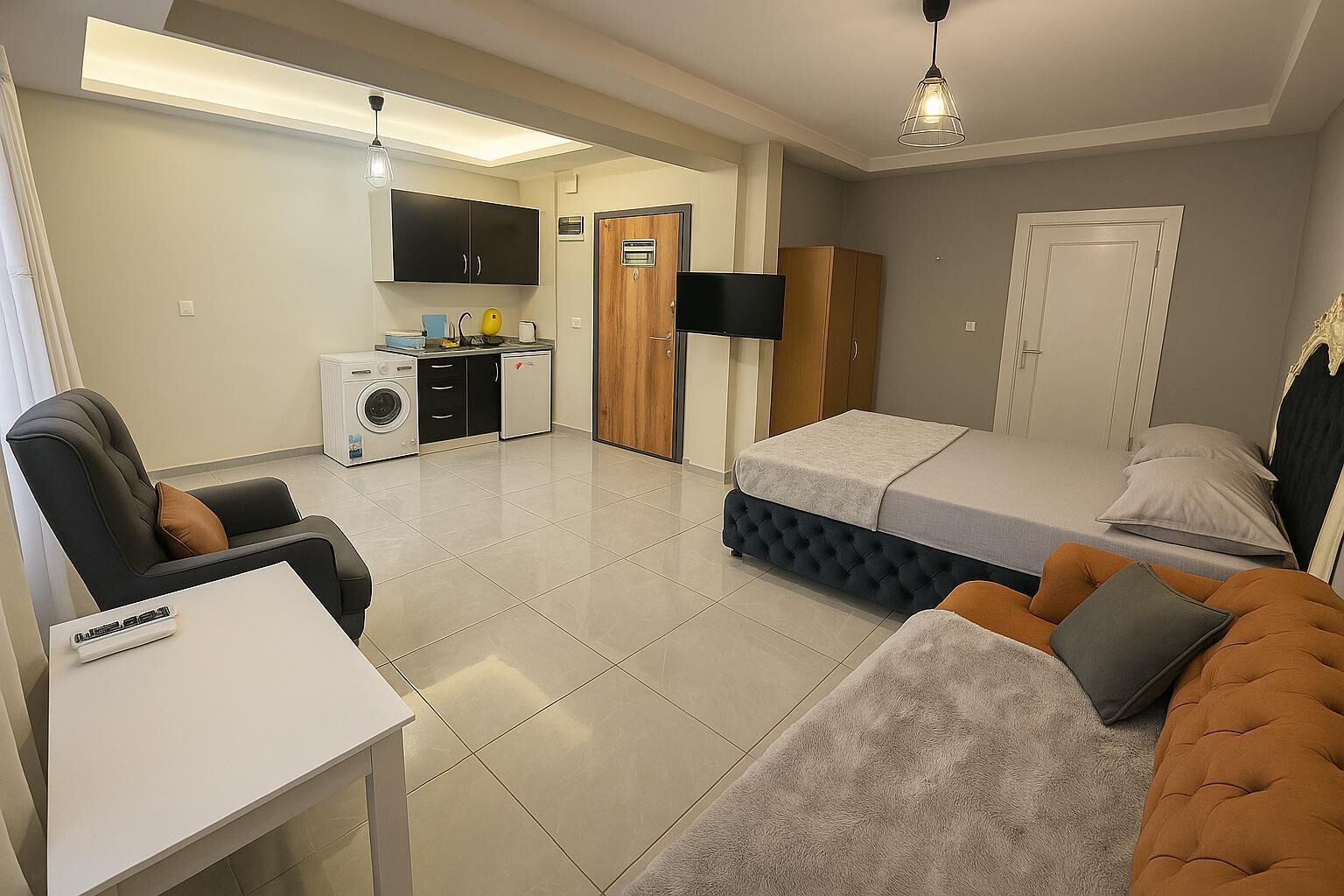 A compact hotel room with a bed, a sofa, a small table, a TV, a washing machine, and a wardrobe.