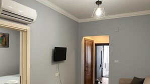 A modern living room with a sofa, a small table, a mounted TV, and an air conditioning unit.