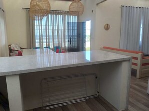 Eine moderne Küche mit Kochinsel, Essbereich mit Stühlen und einem großen Fenster mit Vorhängen.