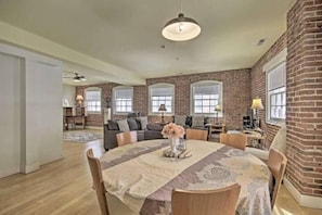 A spacious living room with a brick wall, a round dining table with chairs, and a ceiling fan.