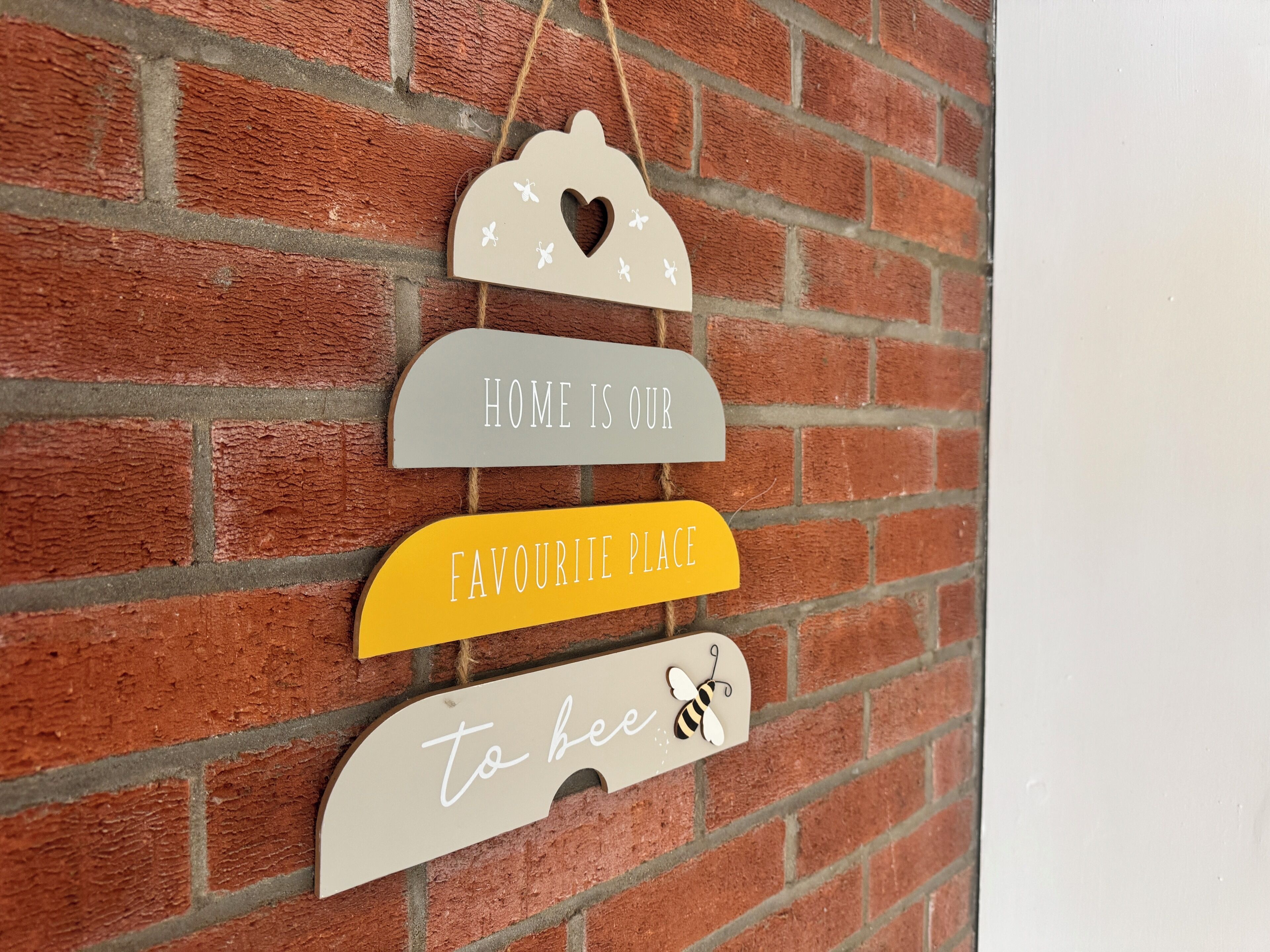 A wall-mounted sign with the text 'HOME IS OUR FAVOURIE PLACE to bee' against a brick wall.