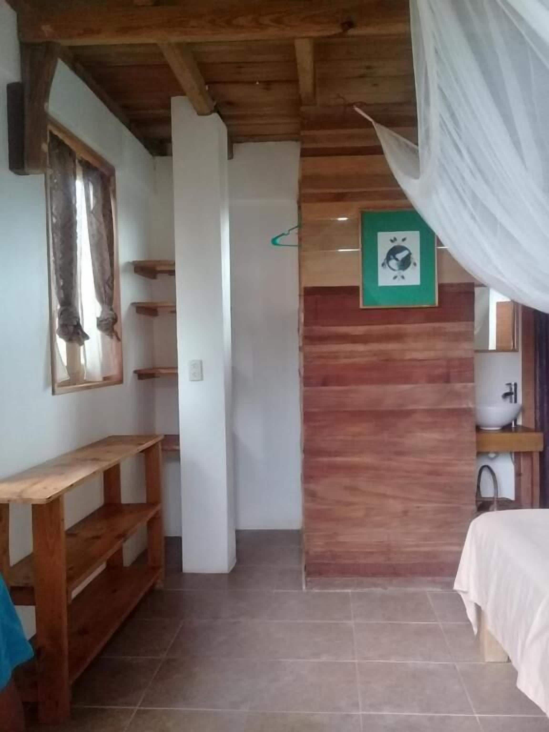 Une pièce avec un plafond en bois, un lit recouvert d’une courtepointe blanche, une horloge murale et une petite étagère.