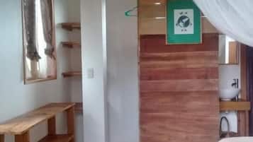 A room with a wooden ceiling, a bed with a white bedspread, a wall clock, and a small shelf.