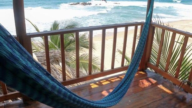 A hammock on a wooden deck overlooking the ocean with waves and a sandy beach. - Casa Acalli Ocean View (San Pedro Pochutla)