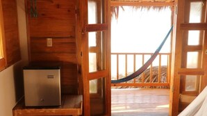 A wooden room with a small refrigerator, a hammock, and a view of a thatched-roof structure. - Casa Acalli Ocean View (San Pedro Pochutla)