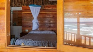 A wooden cabin room with a bed, a mosquito net, and a view of the ocean. - Casa Acalli Ocean View (San Pedro Pochutla)