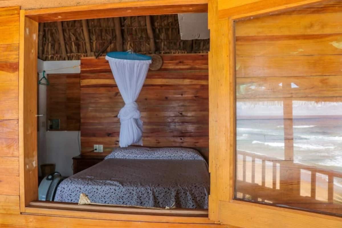 A wooden cabin room with a bed, a mosquito net, and a view of the ocean.