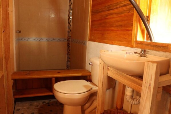 A small bathroom with a toilet, a wooden sink, and a shower area. - Casa Acalli Ocean View (San Pedro Pochutla)
