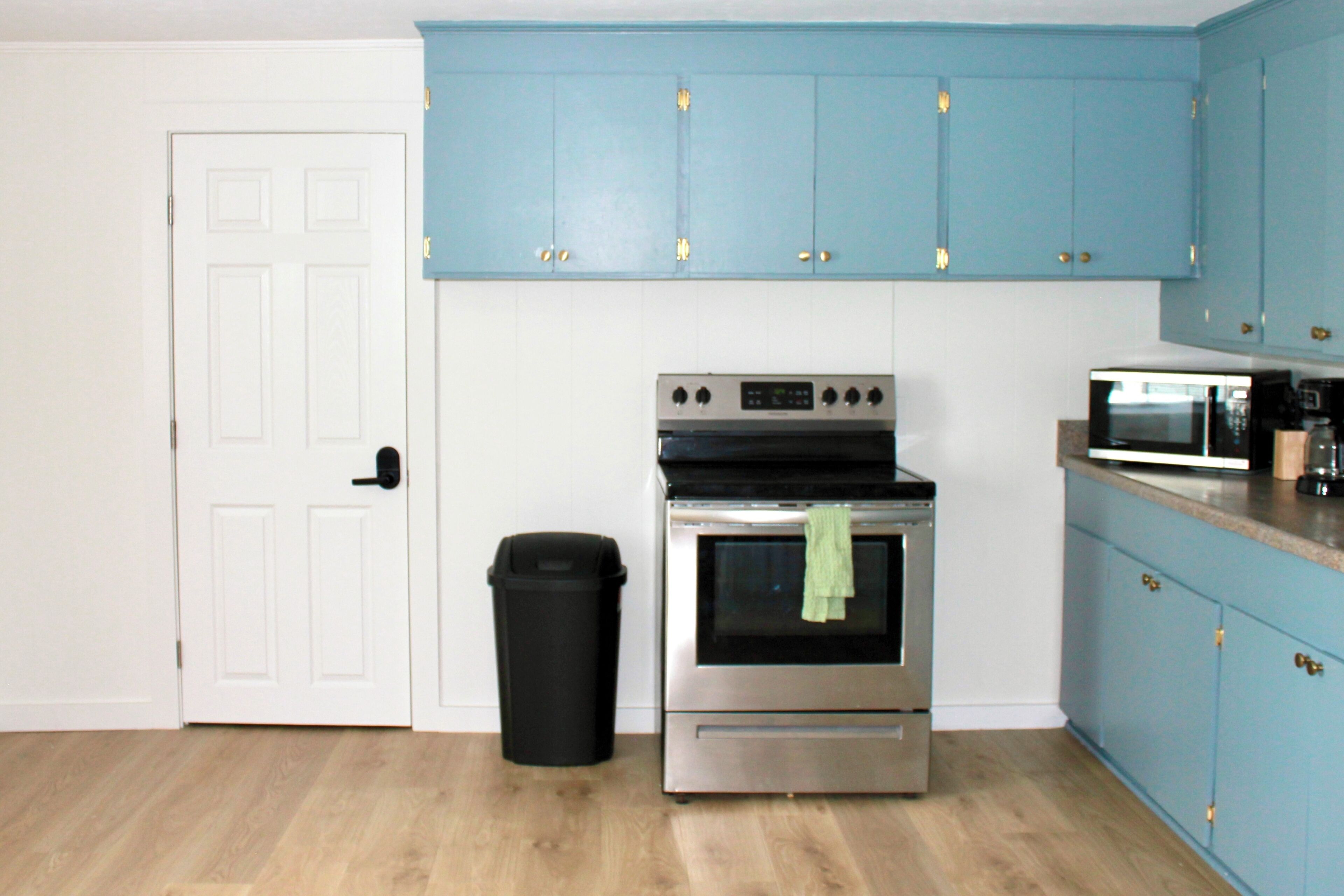 A kitchen with a stainless steel oven, a microwave, and blue cabinets.