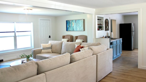 A living room with a sectional sofa, a kitchen with blue cabinets, and a door leading to another room. - Cozy Steinhatchee Getaway, Beachy + River Close (Steinhatchee)