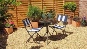 A patio with a wooden fence, two folding chairs, a small round table, and potted plants. - Charming Victorian Garden Apartment | Private Kitchen & Bathroom | King Bed (Southampton)