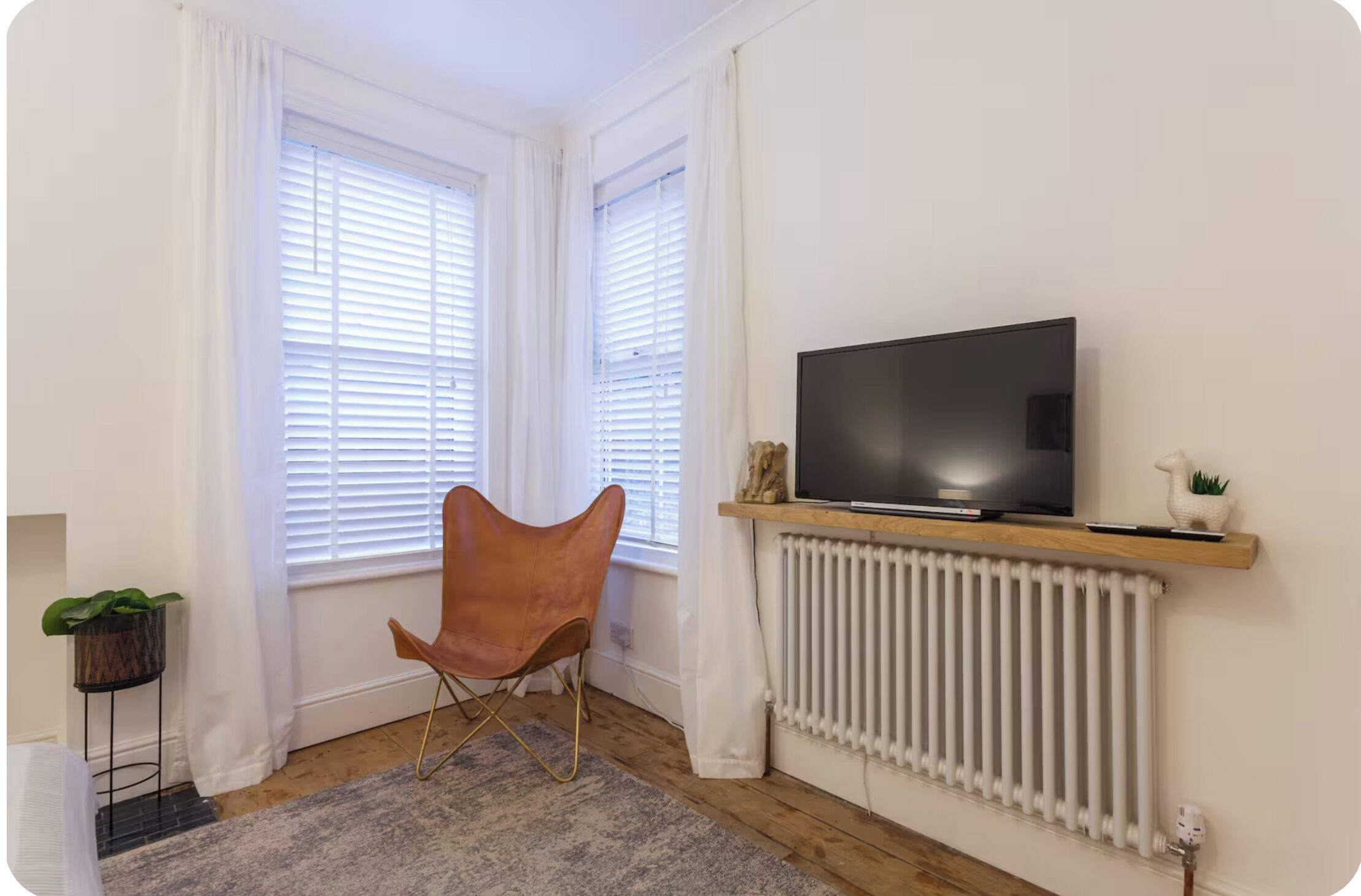 A room with a TV on a wooden shelf, a radiator, a chair, and a plant.