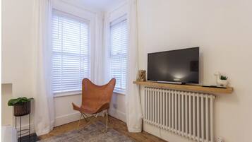 A room with a TV on a wooden shelf, a radiator, a chair, and a plant.