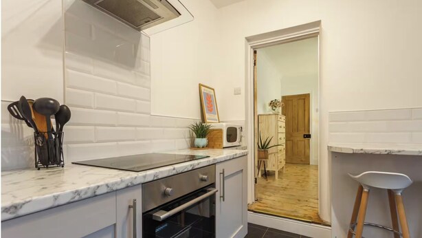 A modern kitchen with white cabinetry, a black oven, a marble countertop, and a wooden stool. - Charming Victorian Garden Apartment | Private Kitchen & Bathroom | King Bed (Southampton)