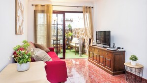 Un salon comprenant un canapé, un téléviseur, un meuble et une petite table sur laquelle est posée une plante.