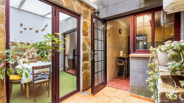 Une terrasse avec une table et des chaises, un mur en pierre et une porte donnant sur un espace intérieur.