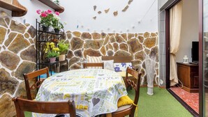 Une pièce aux murs de pierre, avec une table, des chaises, une plante en pot et un téléviseur.