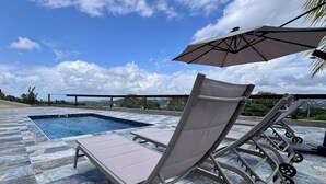Zona de piscina con sillones de descanso y una sombrilla, cielo despejado y vistas del paisaje.