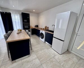A compact kitchen with a washing machine, a refrigerator, and a dining area with a table and chairs. - Apartment F3 Blueberry heated pool Domaine Béthanie (Rivière-Salée)