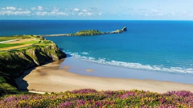 Un paisaje costero con playa, acantilados y una isla en la distancia.