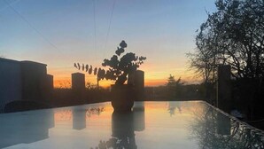 Un área de piscina tranquila al aire libre con vista despejada al atardecer, rodeada de árboles y edificios.