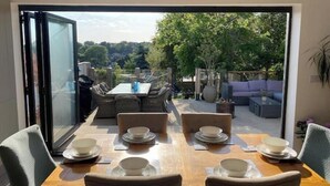 Comedor con una mesa dispuesta para seis, puerta corrediza de vidrio que da a un patio exterior con asientos y vista a follaje.