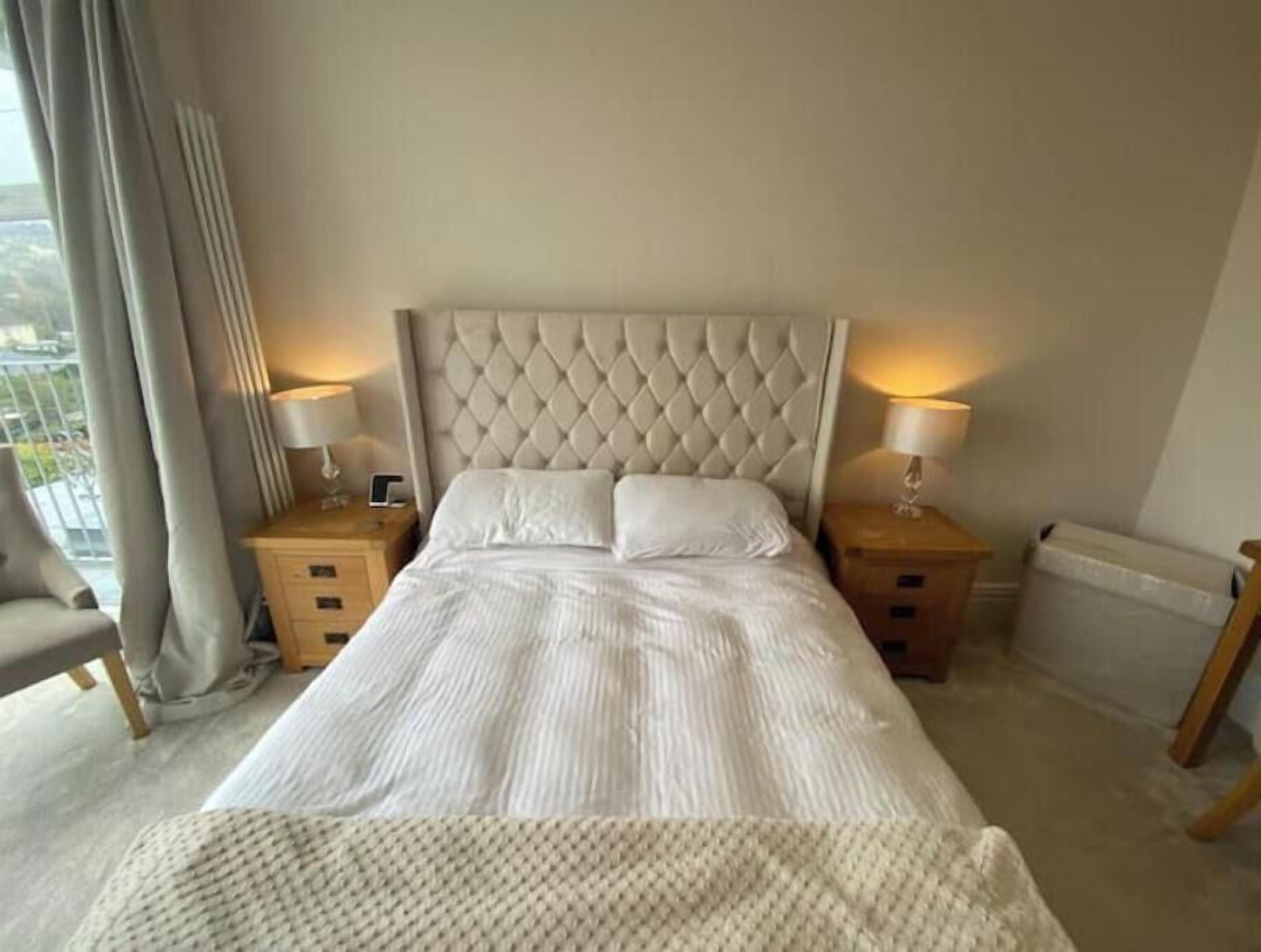 Une chambre d’hôtel avec un grand lit, deux tables de chevet avec des lampes, une chaise et une vue sur l’extérieur.