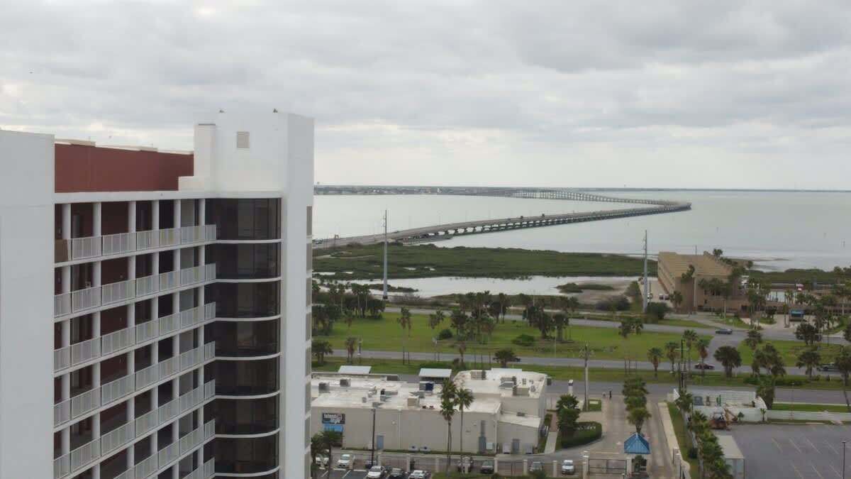 A high-rise building with multiple balconies overlooking a coastal area with a bridge and a marina.