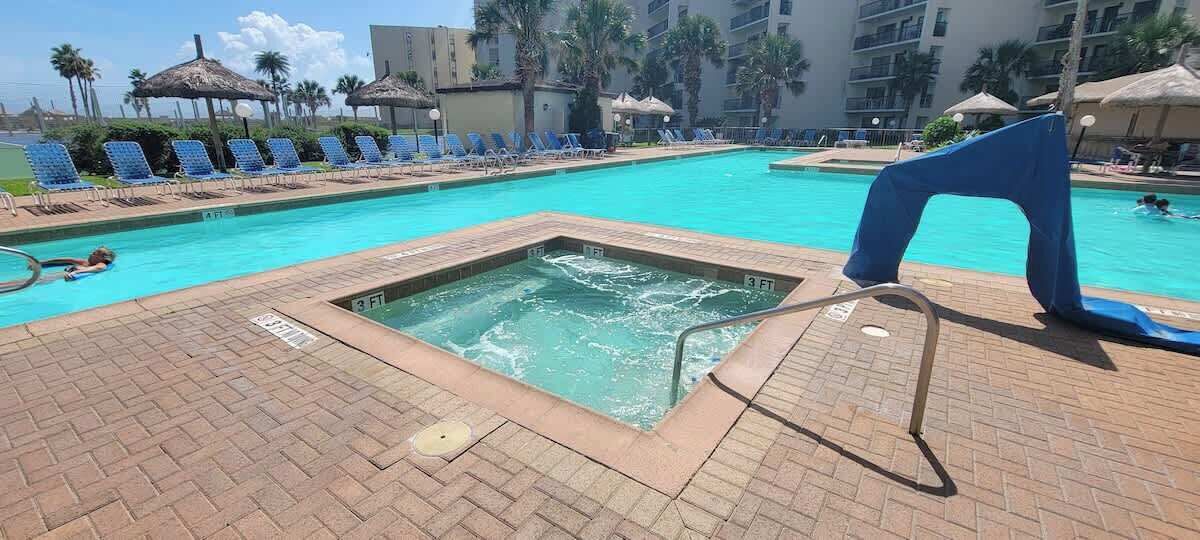 A swimming pool with a hot tub, lounge chairs, and umbrellas.