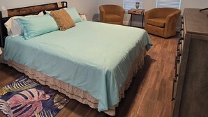 Un dormitorio con cama, dos sillones, una mesita y un aparador.