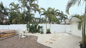 Un patio con suelo de ladrillo, mobiliario exterior blanco y cerca blanca.
