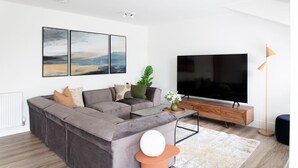 Ein modernes Wohnzimmer mit einer Eckcouch, einem Flachbildfernseher und Kunstwerken an der Wand.