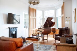 A living room with a grand piano, leather sofas, a fireplace, and large windows.