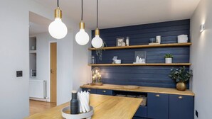 A modern kitchen with wooden cabinets, a dining table, pendant lights, and decorative items on shelves. - Stunning 2 bed flat with parking and garden (Crieff)