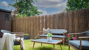A backyard with a wooden fence, a sofa, two chairs, a small table, and potted plants. - Stunning 2 bed flat with parking and garden (Crieff)