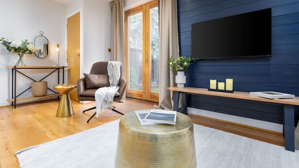 A modern living room with a sofa, a coffee table, a TV mounted on a dark wall, and a wooden floor. - Stunning 2 bed flat with parking and garden (Crieff)