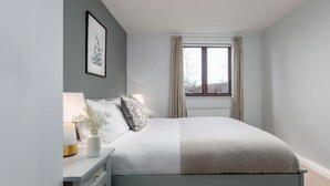 A bedroom with a bed, bedside table, lamp, and a window with curtains. - Stunning 2 bed flat with parking and garden (Crieff)