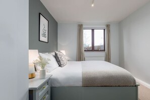 A bedroom with a bed, bedside table, lamp, and a window with curtains. - Stunning 2 bed flat with parking and garden (Crieff)
