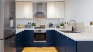 A modern kitchen with dark blue cabinets, a stainless steel refrigerator, a built-in oven, a gas stove, and a sink with a faucet. - Stunning 2 bed flat with parking and garden (Crieff)