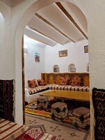 Una habitación con un banco de madera bajo, cojines estampados y una mesita con una naranja.