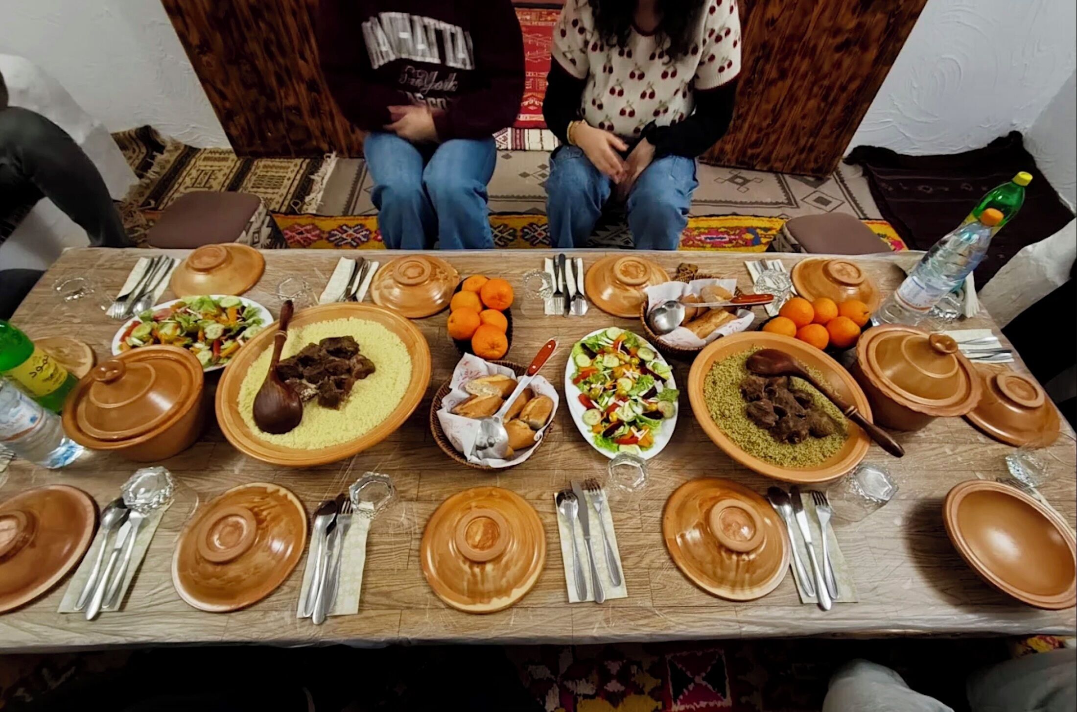 Une table à manger dressée avec différents plats, couverts et une bouteille d’eau.