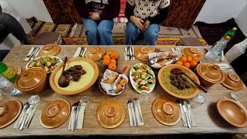 Une table à manger dressée avec différents plats, couverts et une bouteille d’eau.