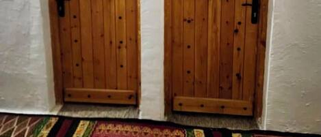Dos puertas arqueadas de madera con manijas metálicas, paredes blancas con textura y una alfombra estampada.