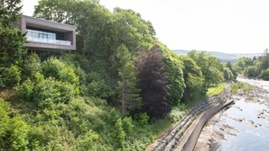 A modern building with a balcony overlooking a river and dense greenery. - Design-led Apartment | Central Pitlochry (Pitlochry)