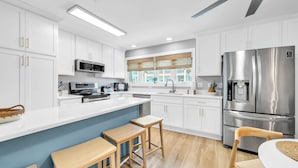 Una cocina moderna con armarios blancos, electrodomésticos de acero inoxidable, una isla grande con taburetes y vistas al exterior.