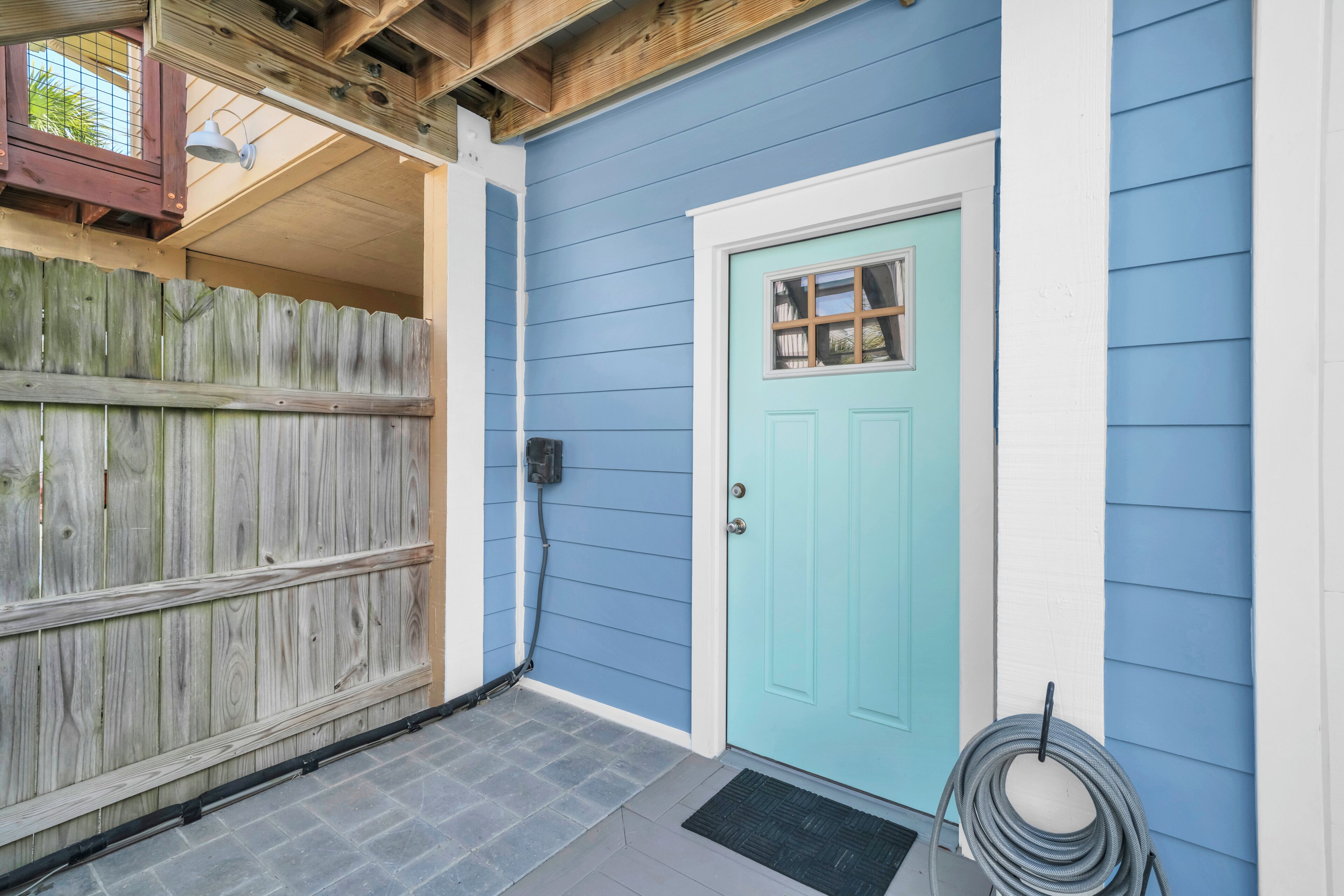 Una casa con fachada azul, puerta azul claro, cerca de madera y felpudo negro.