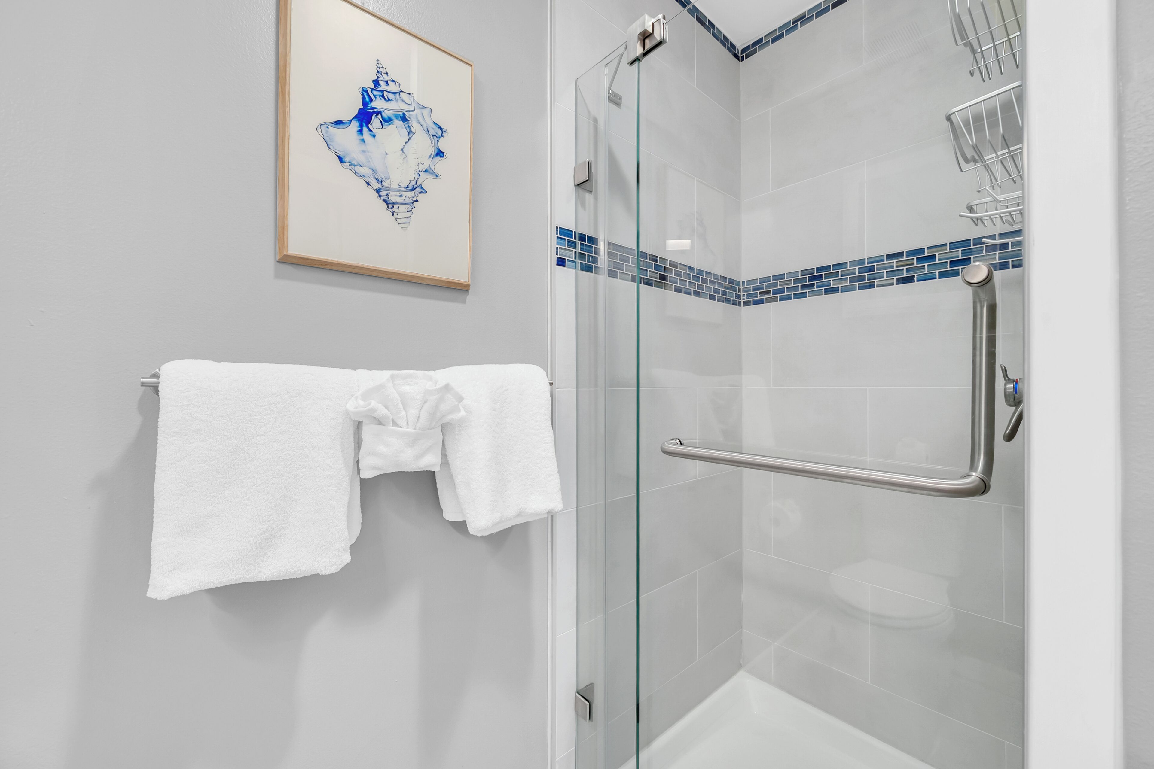 Un baño moderno con cabina de ducha de vidrio, toallero blanco y detalle de mosaico azul.