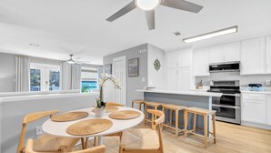 Una cocina moderna con armarios blancos, horno empotrado y zona de comedor con una mesa redonda y sillas de madera.
